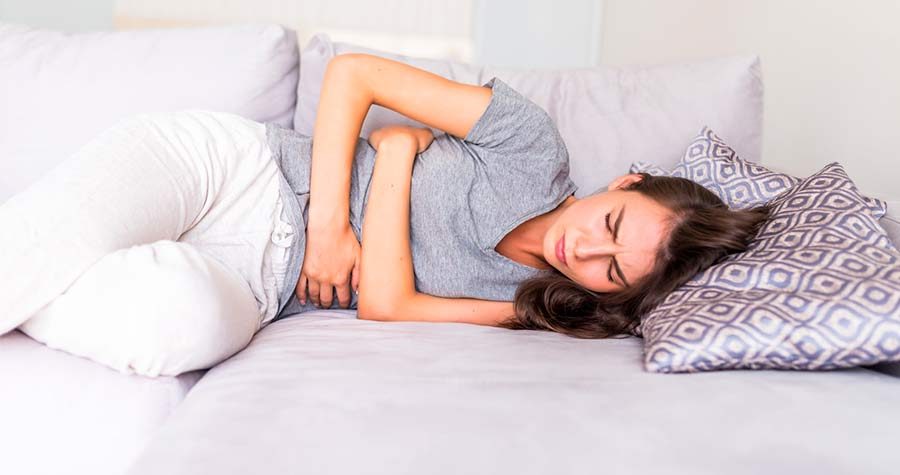 Jovem deitada no sofá, com dores abdominais, um típico sintoma do cálculo renal.