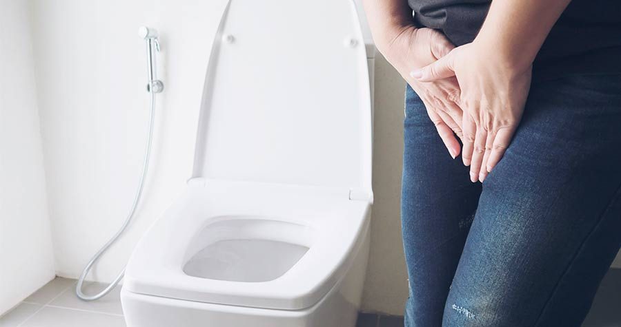 Mulher no banheiro sinalizando que está com dor de bexiga, ou precisando urinar. Estes são sintomas típicos da bexiga hiperativa.